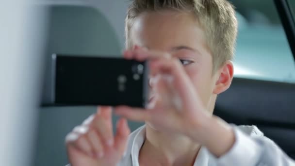 αγόρι που παίζει με ένα έξυπνο τηλέφωνο, σε ένα σύγχρονο αυτοκίνητο - Πλάνα, βίντεο