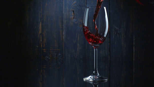Gieten van rode wijn in het glas tegen donkere houten achtergrond. Slow motion - Video