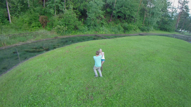 boy and girl spinning on grass with water around - Footage, Video