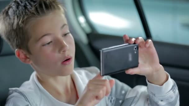 boy playing with smartphone camera in back of a car - Footage, Video