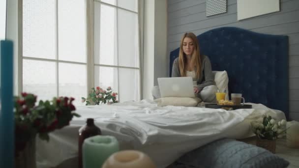 Kız bir yatakta bir dizüstü bilgisayar ve kahvaltı ile çalışma - Video, Çekim