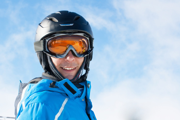 Homme souriant dans la veste de ski bleue, casque et lunettes contre ciel nuageux
 - Photo, image