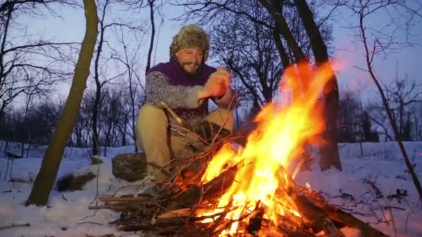 Bearded man warming his hands by the fire in winter. Tourist man evening campfire. A young bearded man at a fire in the woods. - Felvétel, videó