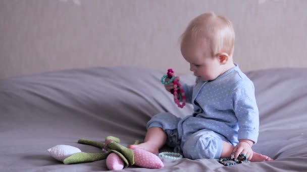 A baby on a bed sitting and playing with brecelets - Záběry, video