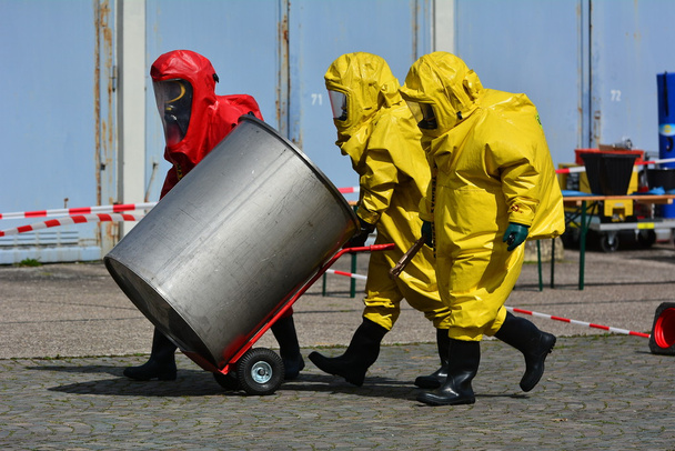 Werknemer in beschermende uniforme, masker, handschoenen en laarzen vervoer vaten van chemische stoffen - Foto, afbeelding
