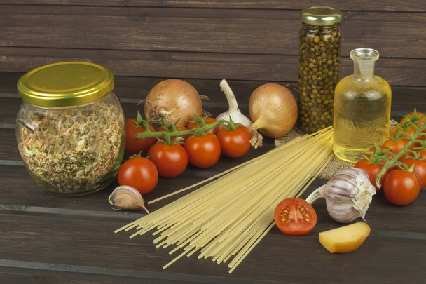 Preparing homemade pasta. Pasta and vegetables on a wooden table. Dietary food. Pasta, tomatoes, onion, olive oil and basil on wooden background. - Fotó, kép