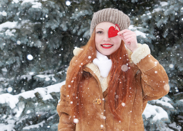 Fiatal nő pózol, piros szív játék. Téli szezonban. Kültéri álló parkban. Havas időjárás. Valentin koncepció. - Fotó, kép