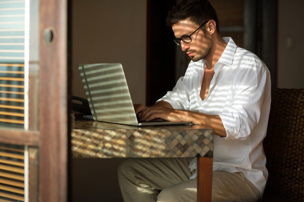Young businessman sitting at desk, using laptop - 写真・画像