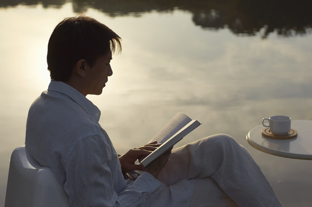 hombre leyendo libro al lado del lago en la mañana
 - Foto, imagen