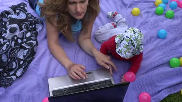 Bébé enfant interrompre mère travailler avec ordinateur sur plaid dans le jardin. 4K
 - Séquence, vidéo