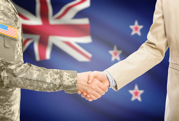 USA military man in uniform and civil man in suit shaking hands with national flag on background - New Zealand - Fotografie, Obrázek