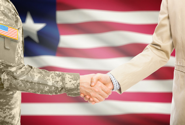 США военный человек в военной форме и гражданской мужчина в костюме, рукопожатие с национальным флагом на фоне - Либерия - Фото, изображение