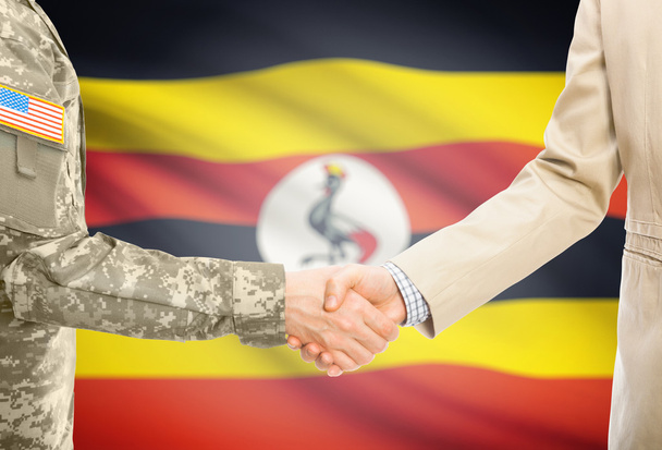 USA military man in uniform and civil man in suit shaking hands with national flag on background - Uganda - Fotografie, Obrázek