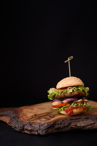 Delicious homemade burger on rustic wooden board, dark background. Copy space. - Foto, Imagen