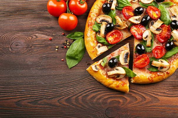 Sliced delicious tasty pizza with vegetables on wooden table - Фото, зображення