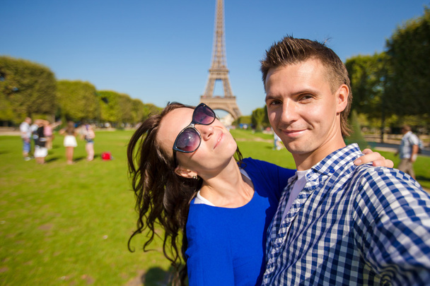Young happy family taking self portrait in Paris background the Eiffel Tower. Young adults holding smartphone camera to take a picture of themselfes during summer vacation in Europe - Photo, Image