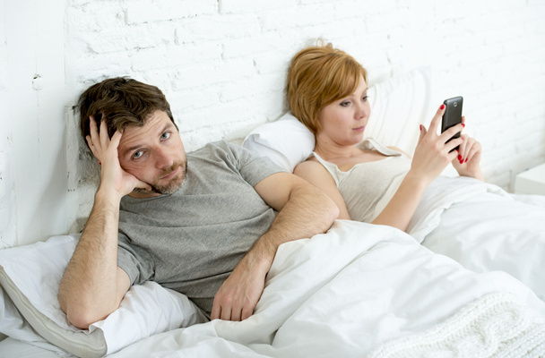 couple in bed husband frustrated upset unsatisfied while wife using mobile phone  - Foto, Bild