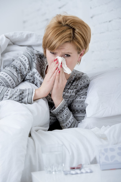 mulher com espirros nariz soprando no tecido na cama sofrendo sintomas do vírus da gripe fria ter medicamentos comprimidos comprimidos
 - Foto, Imagem