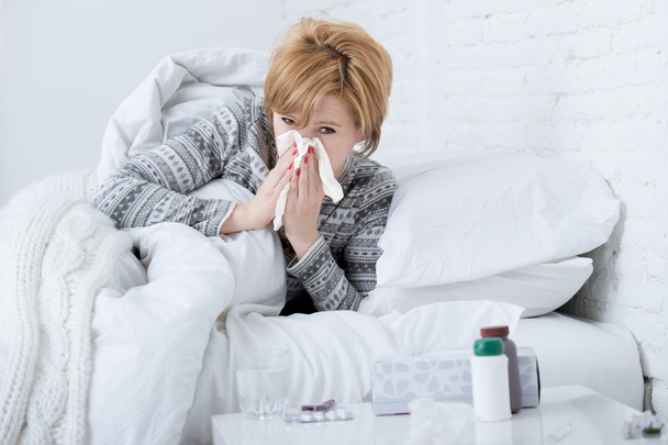 woman with sneezing nose blowing in tissue on bed suffering cold flu virus symptoms having medicines tablets pills - Photo, Image