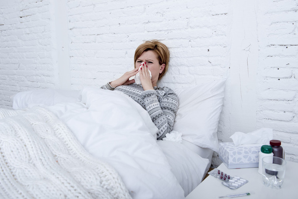 woman with sneezing nose blowing in tissue on bed suffering cold flu virus symptoms having medicines tablets pills - Photo, Image