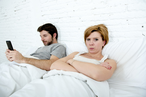 young couple in bed unsatisfied wife bored frustrated and angry while internet addict husband is using mobile phone  social network obsession - Фото, зображення