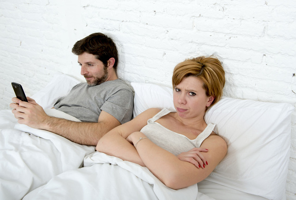 mladý pár v posteli neuspokojené manželky frustrovaný, zatímco internet addict manžel používá mobilní telefon sociální sítě posedlost - Fotografie, Obrázek
