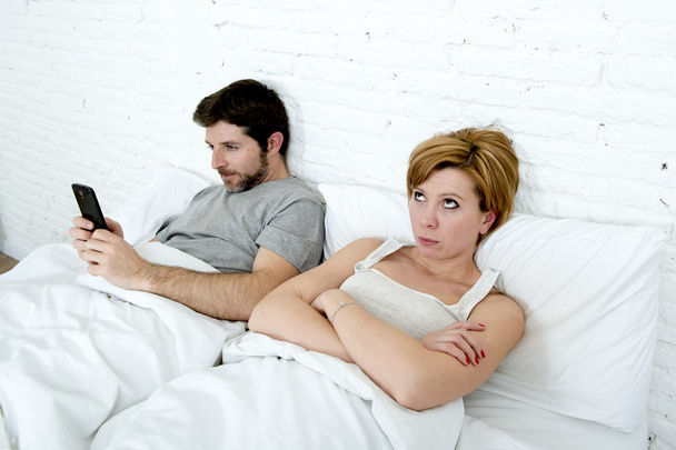 молодая пара в постели неудовлетворенная жена скучно разочарованы и сердиты в то время как интернет-наркоман муж использует мобильный телефон социальной сети одержимость
 - Фото, изображение