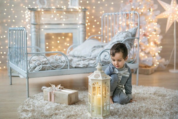 A cute boy looks at the lantern near the bed - Foto, afbeelding