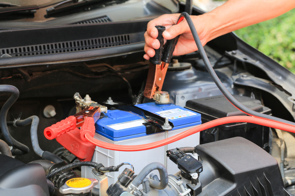 Car mechanic uses battery jumper cables charge a dead battery. - Photo, Image
