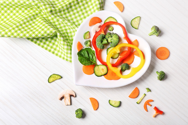 Useful cut vegetables on a plate in the form of heart on wooden table top view - Foto, afbeelding