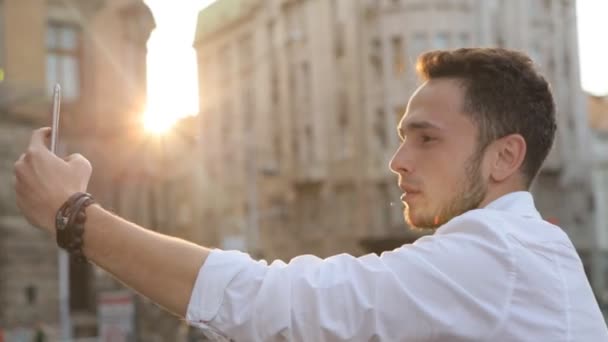 Młody człowiek biorąc panorama obraz za pomocą jego smartphone. Przystojny kaukaski mężczyzna w jego 20s robi selfie na zewnątrz. Facet za pomocą przedniego aparatu na jego urządzenie. - Materiał filmowy, wideo