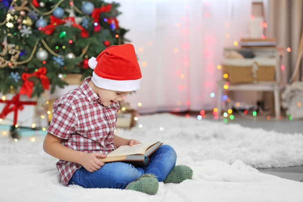 Cute small kid reading book on Christmas tree background - Photo, image