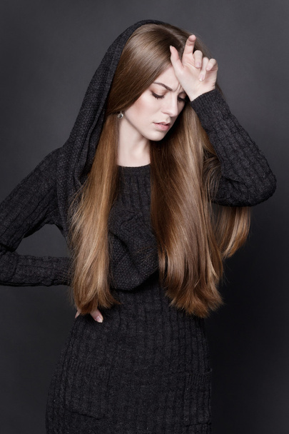 Молодая привлекательная женщина с длинными, великолепными темными светлыми волосами. Она одета в теплое серое вязаное платье
 - Фото, изображение