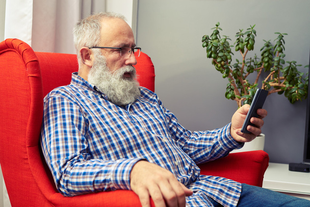 senior man resting on the chair with smartphone - Zdjęcie, obraz
