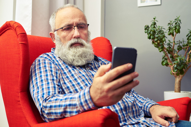 Mann mit Brille sitzt mit Smartphone auf dem Stuhl - Foto, Bild