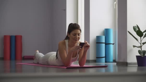 Ragazza sdraiata sul tappetino yoga e guardando il telefono
. - Filmati, video