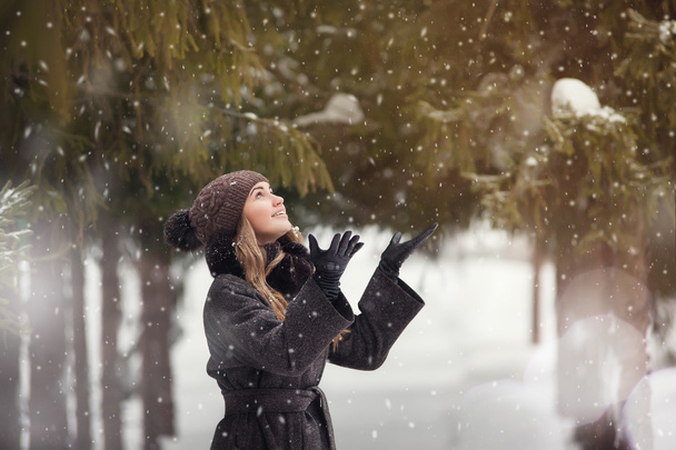young beautiful woman in the park enjoys snowfall - Фото, изображение