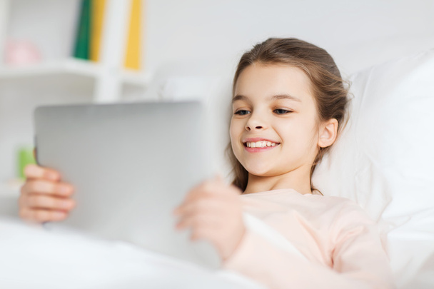 happy girl lying in bed with tablet pc at home - Foto, imagen