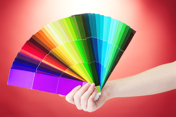 ruka držící světlé palety barev na červeném pozadí - Fotografie, Obrázek