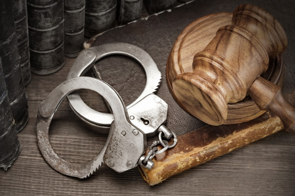 手錠、裁判官小槌と木製のテーブルの古い法律の本 - 写真・画像
