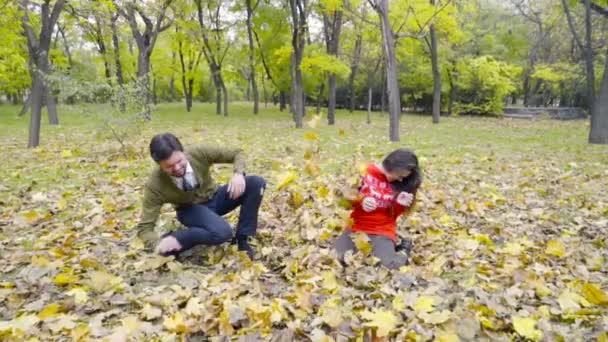 Młoda para rzucanie się liści w parku zwolnionym tempie - Materiał filmowy, wideo