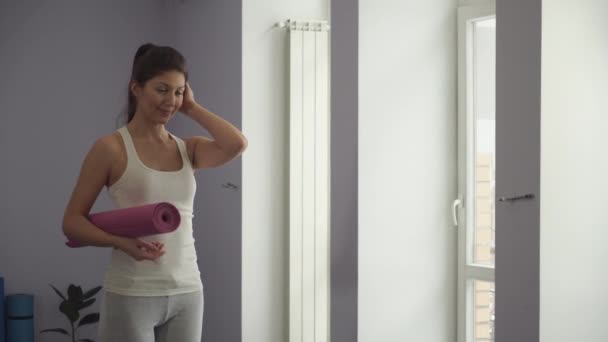 Девушка, стоящая с ковриком для йоги, готовится к тренировке
. - Кадры, видео