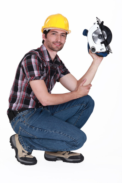 Man crouching down whilst holding circular saw - Фото, изображение