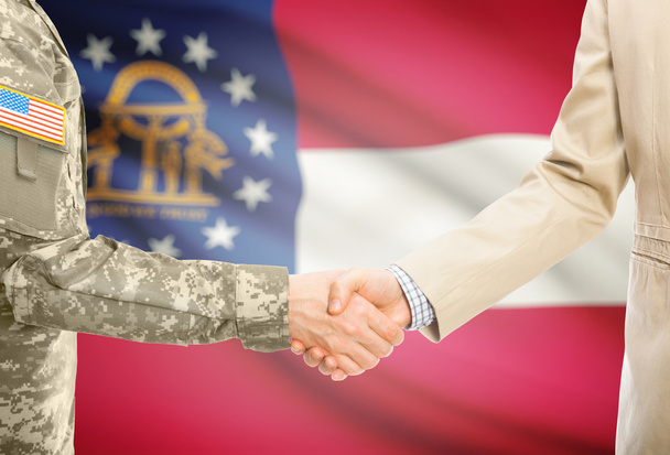 USA military man in uniform and civil man in suit shaking hands with USA state flag on background - Georgia - Fotografie, Obrázek