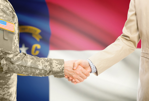США военный человек в военной форме и гражданской мужчина в костюме, рукопожатие с США государственный флаг на фоне - Северная Каролина - Фото, изображение
