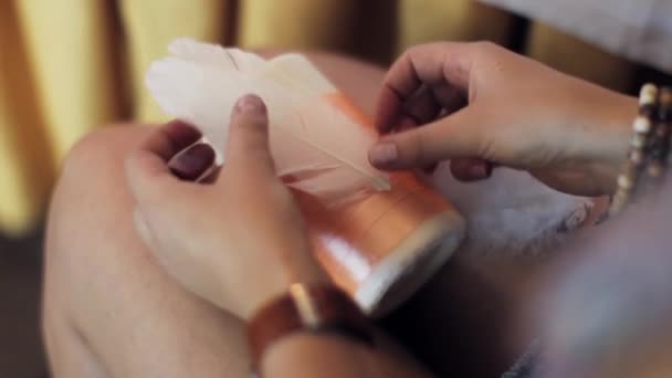 Womans kezek ragasztó fehér tollak a nagy gyertya térdre narancssárga szalaggal. - Felvétel, videó