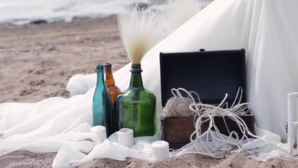 Decorative bottles stand on white tissue with candles, box of threads. Beach. - Footage, Video