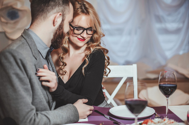 Beautiful young couple with glasses of red wine in luxury restaurant - 写真・画像