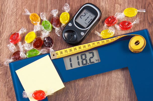 Escala electrónica de baño y glucosímetro con resultado de medición y coloridos caramelos, diabetes, adelgazamiento y reducción de comer dulces
 - Foto, imagen