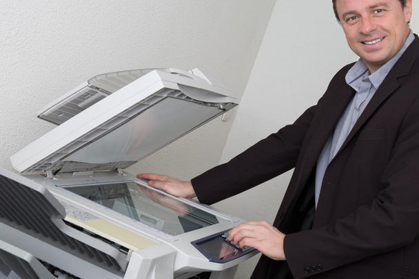 Homme d'affaires joyeux avec les bras sur l'imprimante regardant la caméra
 - Photo, image